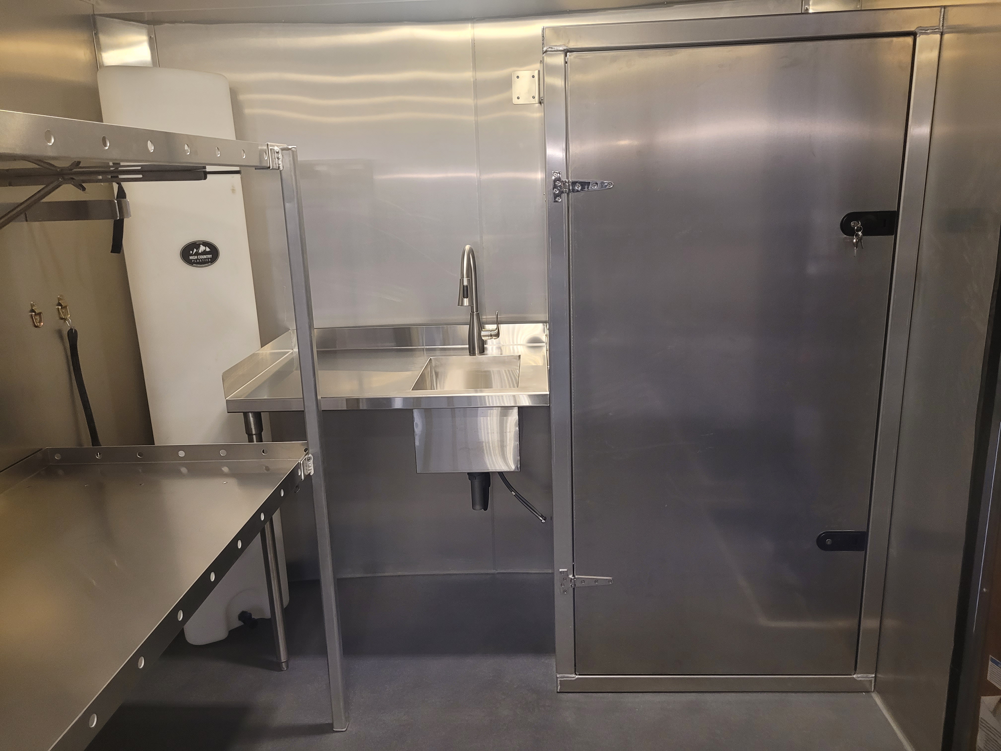 Interior of a custom stainless steel trailer with sink and shelving